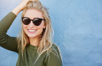 cheerful blonde in sunglasses smiling on blue background